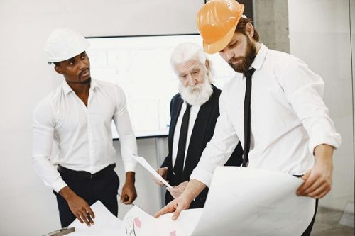 Architects wearing protective helmets examining construction blueprints on site during project planning.