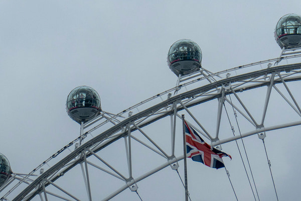 United Kingdom flag fluttering on a flagpole against the London Eye.