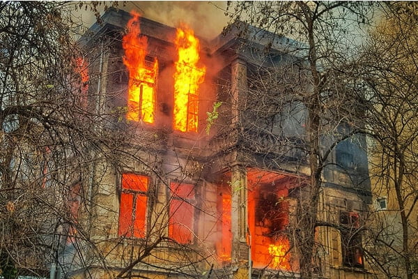 Residential house on fire surrounded by trees, illustrating the severity of property damage risks.